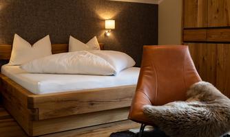 A modern bedroom with a large bed and two pillows. A cozy armchair and a wooden wardrobe complete the decor.