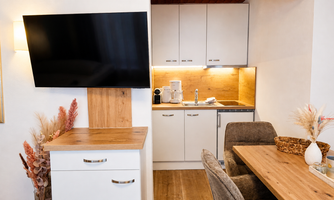 A modern kitchen with a television, a wooden shelf, and a stylish dining table. The interiors are bright and invitingly designed.