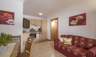 A cozy living room with a red sofa and a dining table. The kitchen is modern and well-equipped, with decorative pictures on the walls.