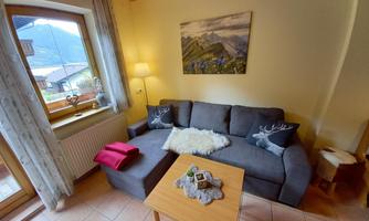 A cozy living room with a gray sofa and a wooden coffee table. The window offers a view of the mountains, and a calm atmosphere is created by the soft lighting.