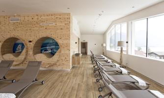 A relaxing wellness area with loungers and large windows. The wooden paneling creates a cozy atmosphere.