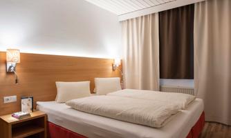 A cozy bedroom with a large bed and light wood design. Soft cushions and gentle lighting create a relaxing atmosphere.