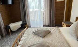 A cozy bedroom with wood paneling and large windows. The bed is decorated with pillows, and a television hangs on the wall.