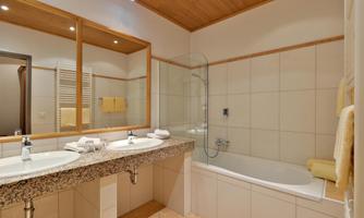 A modern bathroom with two sinks and a bathtub. The walls are tiled in light colors, and a wooden ceiling creates a warm atmosphere.
