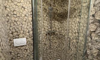 A modern bathroom with a shower cabin and a toilet. The walls are adorned with a decorative stone design.