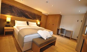 A modern bedroom with two beds and warm wood paneling. The room is bright and stylishly designed, with a small desk and a cozy atmosphere.