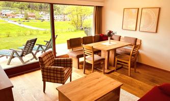 A bright and cozy living room with a dining area and a view of the green landscape. Comfortable furniture and large windows create an inviting atmosphere.