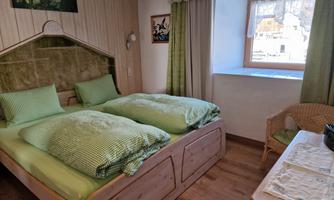 A cozy room with two single beds and green bedding. The room has a window with a view outside and offers a warm atmosphere.