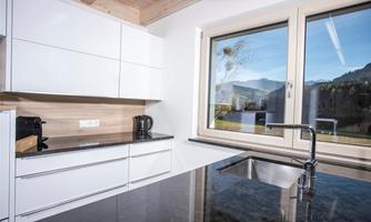 Modern kitchen with white cabinets and a black countertop. Large windows that provide a view of the landscape.