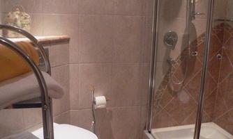 A bathroom with a shower cubicle and a toilet. The walls are tiled and there are some towels on a holder.