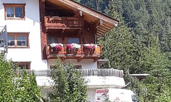 A charming house with balconies, surrounded by trees and mountains. The architecture is traditional and blends well with the landscape.