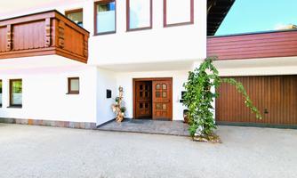 A modern house with a large entrance area and balcony. In front of the front door, there are plants and decorations.