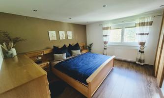A modern bedroom with a large bed and wooden furniture. The windows let in plenty of light and the walls are painted in soft colors.