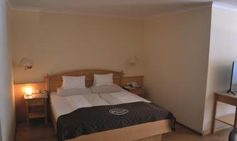 A cozy hotel room with a double bed and bright walls. Next to the bed is a nightstand and a desk.