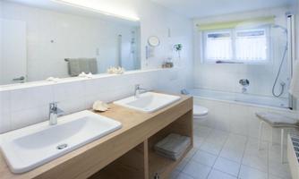A modern bathroom with two sinks and a large mirror. The bathtub and bright light create an inviting atmosphere.