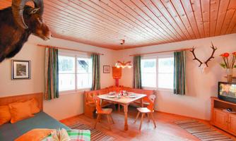 A cozy room with wooden ceilings and a dining table in the center. Antlers and animal heads hang on the wall, while the windows let in plenty of daylight.