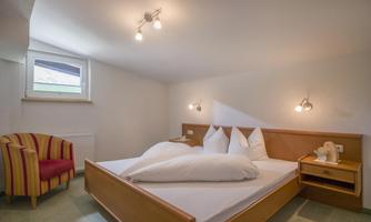 A cozy bedroom with a large bed and bright ceiling lights. A colorful armchair complements the decor.