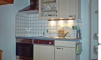 A small, modern kitchen with a stove, an oven, and a sink. The walls are decorated with white tiles, and there are integrated light sources.