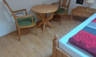A cozy room with a wooden floor. There is a bed, a table with two chairs, and a lamp.