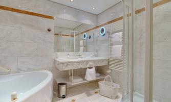 A modern bathroom with marble tiles, a bathtub, and a shower. The room is brightly lit and features an elegant shelf with towels.