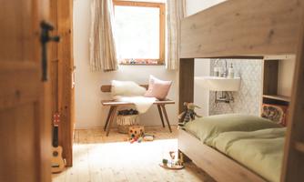 A cozy children's room with a colorful loft bed and a large window. The decor is bright and friendly, with wooden details and toys on the floor.