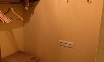 A small room with a wooden chest of drawers and a clothes rack. Two hooks are hanging on the wall.