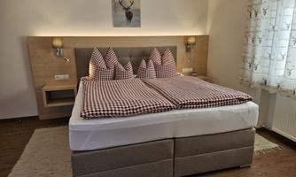 A cozy bedroom with a large bed and checked pillows. The warm lighting and wooden details create a relaxed atmosphere.
