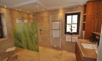 A modern bathroom with a glass shower partition and an elegant sink. The warm wooden elements and the stone tiles create a cozy atmosphere.