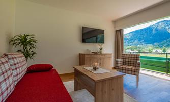A modern living room with a red sofa and a wooden table. A mountain landscape can be seen through the window.