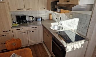 A modern kitchen with wood veneer and glossy appliances. On the countertop, a coffee machine and a kettle can be seen.