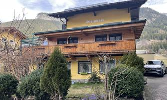 A charming two-story house in yellow with wooden cladding. Surrounded by trees and overlooking the mountains.