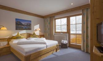 A cozy bedroom with a wooden double bed and soft lighting. Large windows provide plenty of natural light and a view of the mountains.