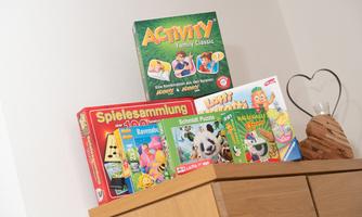 A collection of board games and puzzles on a wooden shelf. Below are games like "Activity" and "Ravensburger".