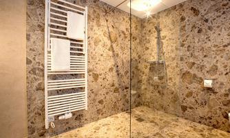 A modern bathroom with stone mosaic walls and a spacious shower. Towels hang on a white towel radiator.