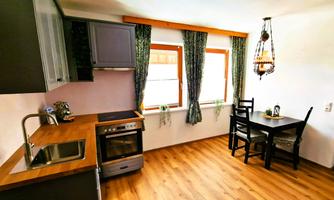 A modern kitchen with a wooden table and chairs. Bright windows with curtains and high-quality kitchen equipment are visible.