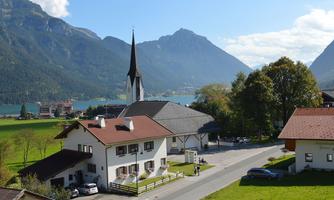 A picturesque landscape with mountains, a clear lake, and traditional houses. In the background, the church tower is visible.