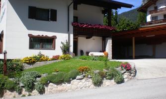 A cozy house with a beautiful garden and colorful flowers. In the background, mountains and a clear blue sky can be seen.