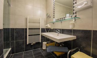 A modern bathroom with a shower and a sink. The walls are light-tiled, and there is a towel warmer.