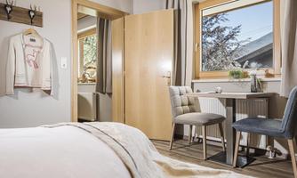 A cozy room with a large bed and a small table. Sunlight streams in through the window, and the space feels bright and inviting.