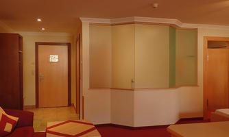A cozy living area with a red carpet and sofas. In the background, there is a wooden door and a bright wall.