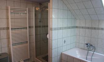 A modern bathroom with a shower and a bathtub. The walls are tiled and there is a towel radiator.