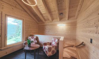 A cozy room with wood paneling, two floral armchairs, and a small table. A large window offers a view of the outdoors.