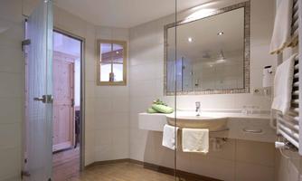 A modern bathroom with a shower and a large mirror. The walls are tiled in light colors, and there are towels as well as plant arrangements.