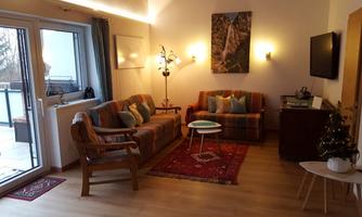 A cozy living room with two sofas and a small table. There is a window leading to a balcony and a small Christmas decoration.