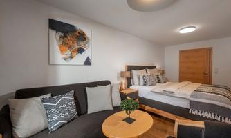 A modern room with a double bed and a cozy seating area. The walls are painted light, and a piece of art hangs above the couch.