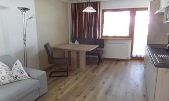 A modern living room with a cozy couch and a dining table. Large windows provide plenty of natural light.