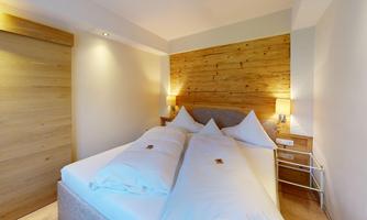 A cozy bedroom with a double bed and wood paneling. The warm lights create an inviting atmosphere.
