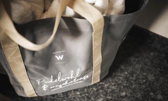 An elegant bag with the print "Poodle Well & Well-being". Inside are some white towels.
