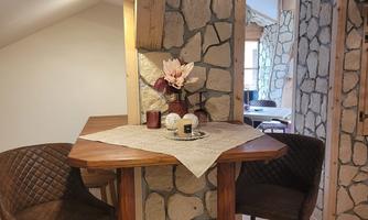 A cozy dining area with a wooden table and two chairs. The walls are clad with stones, and there is a floral decoration on the table.