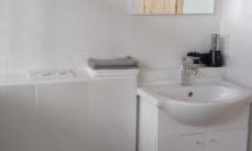 A modern bathroom with white tiles and simple furniture. There is a sink, a toilet, and a mirror.